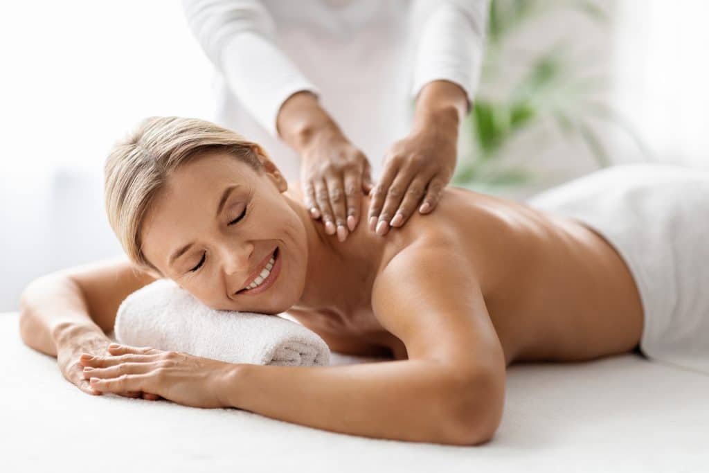 Beautiful middle aged woman receiving relaxing shoulder massage in spa salon